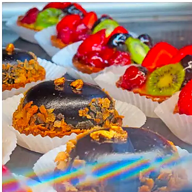 The pastry case at La Sucrière — fruit tarts with kiwi and strawberry beside chocolate-glazed domes