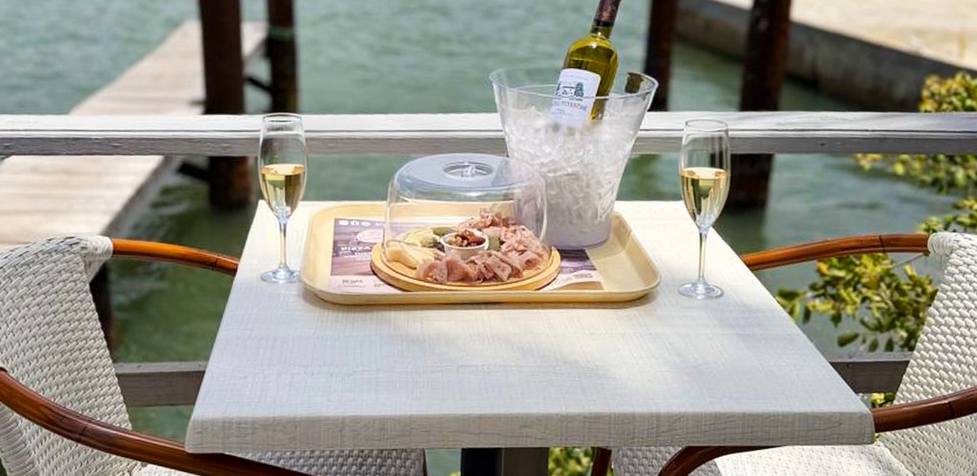 A charcuterie board and chilled wine on a lagoon side table at La Sucriere